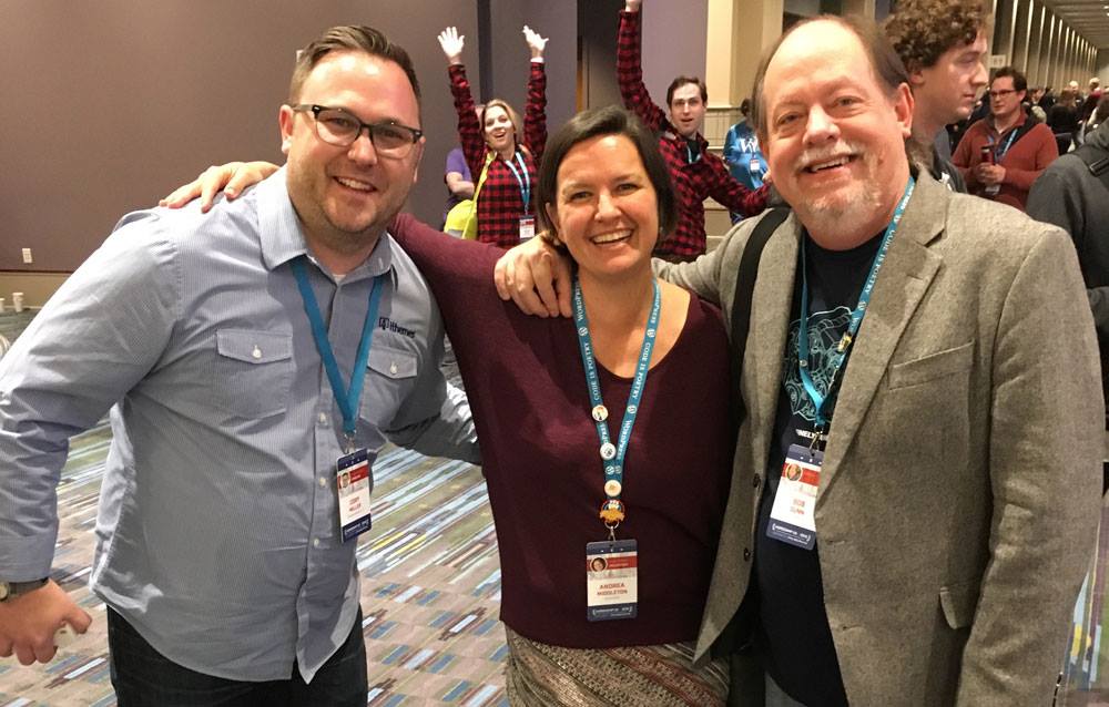 An image of three people smiling, with arms around each other, at a conference. 
